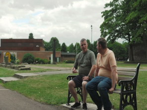 Two man sat on a bench in a park