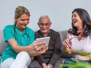 A nurse showing patients something on a tablet device. The patients are smiling.