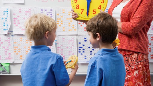 Two boys at primary school learning about time with teacher and clock