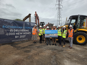 A group of people stood on a building site holding a sign saying 'investing in Rotherham'.