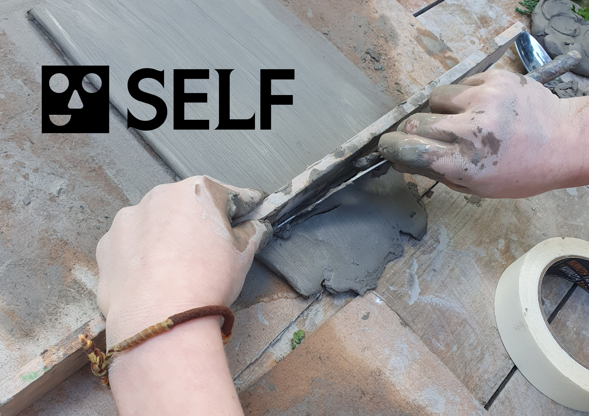 A person measuring grey clay. SELF written in top left corner.