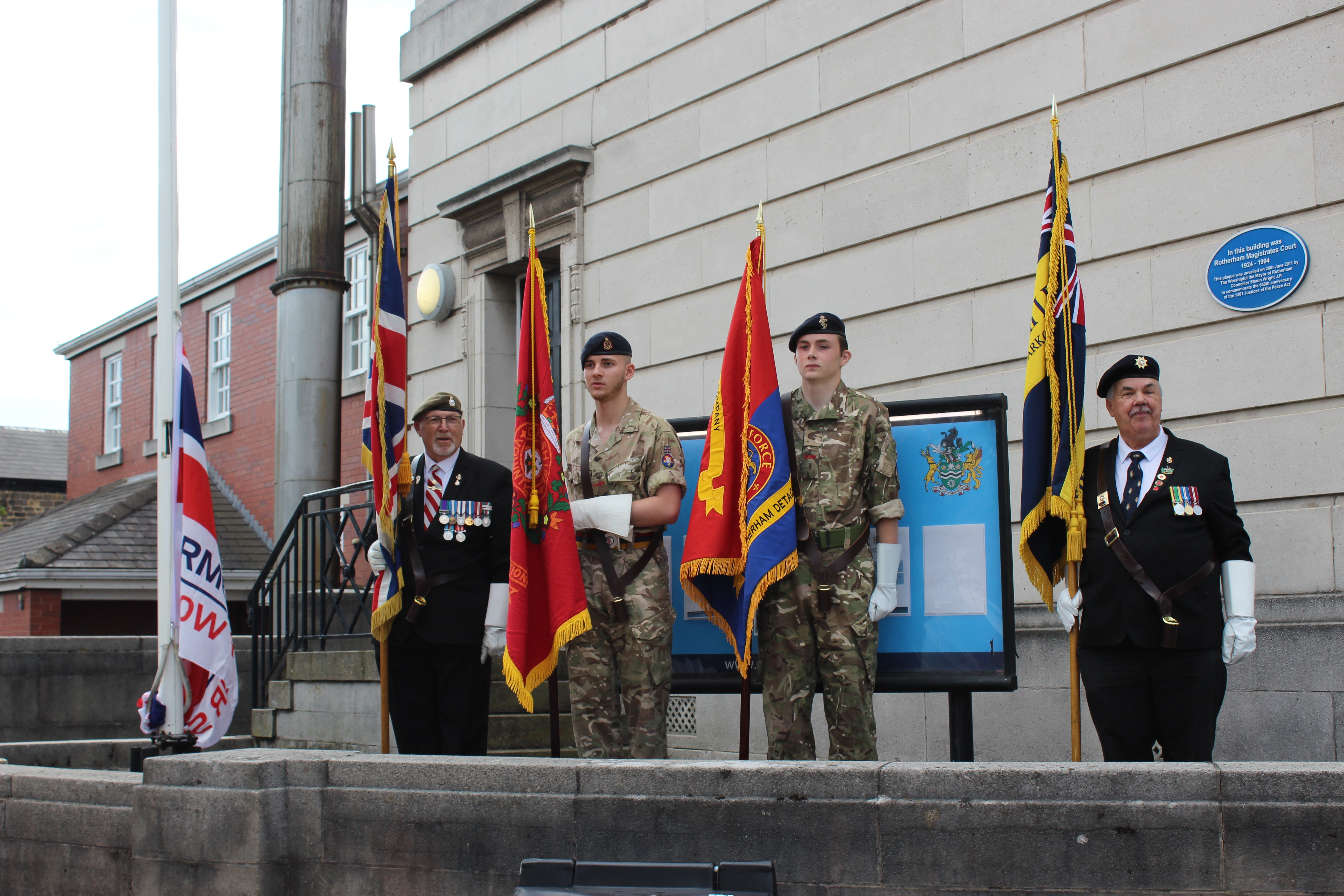 Four stand in front of a building holding flags.