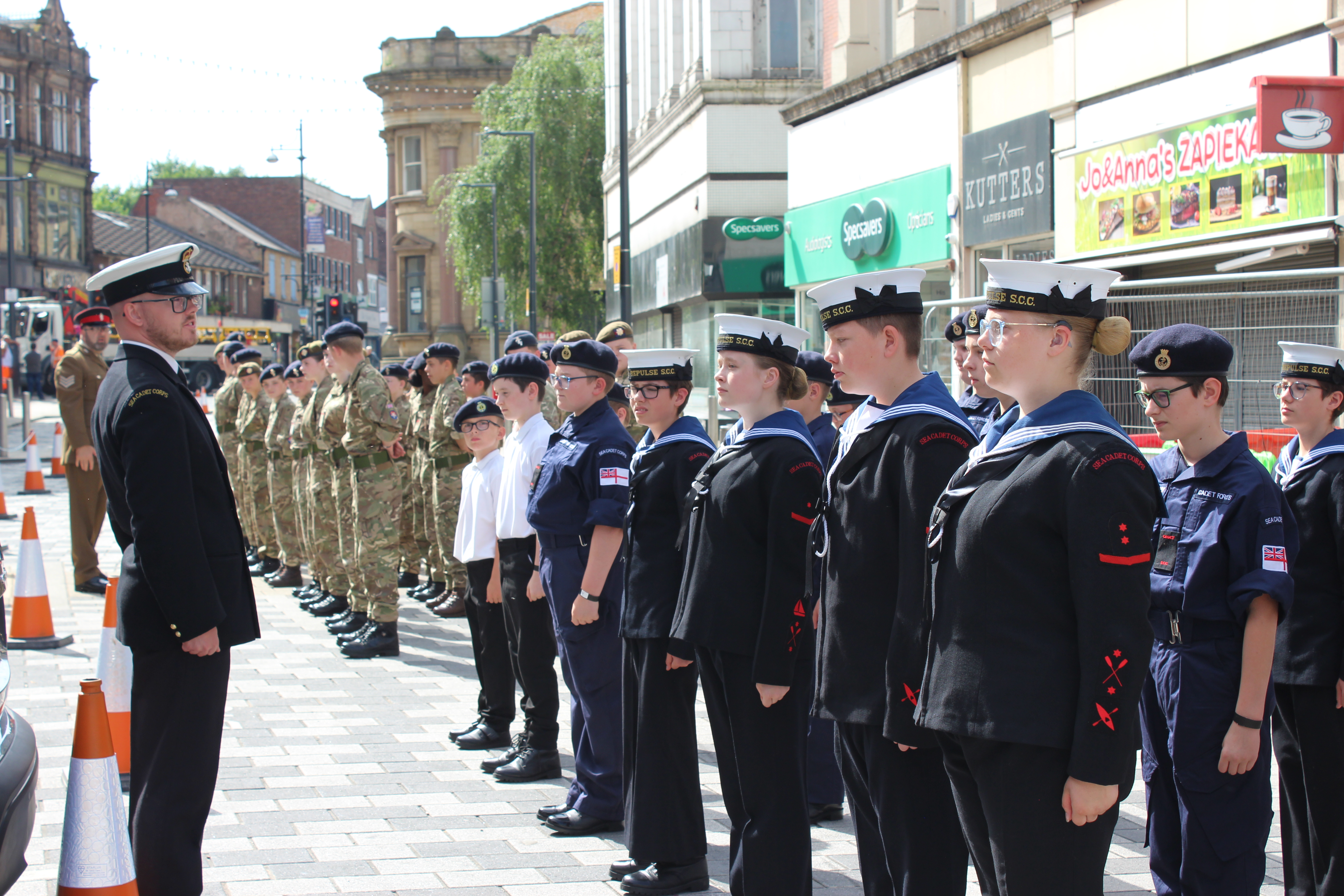 Military in navy uniforms and  camouflage stand in formation.