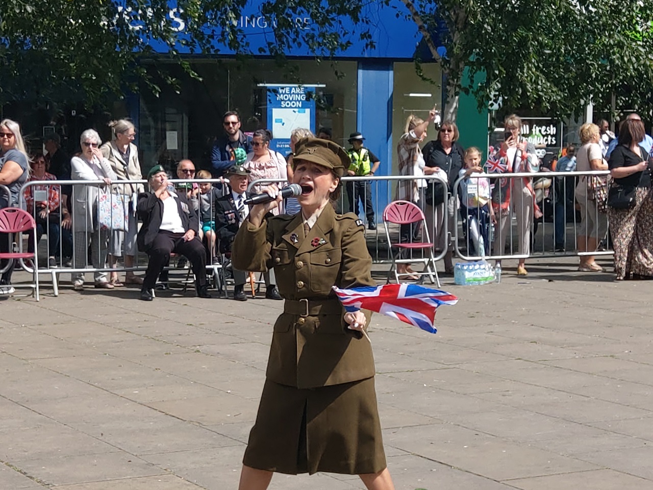Female in army uniform singing holding a union jack flag