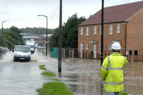 A person in a high-vis jacket standing next to a flooded road.