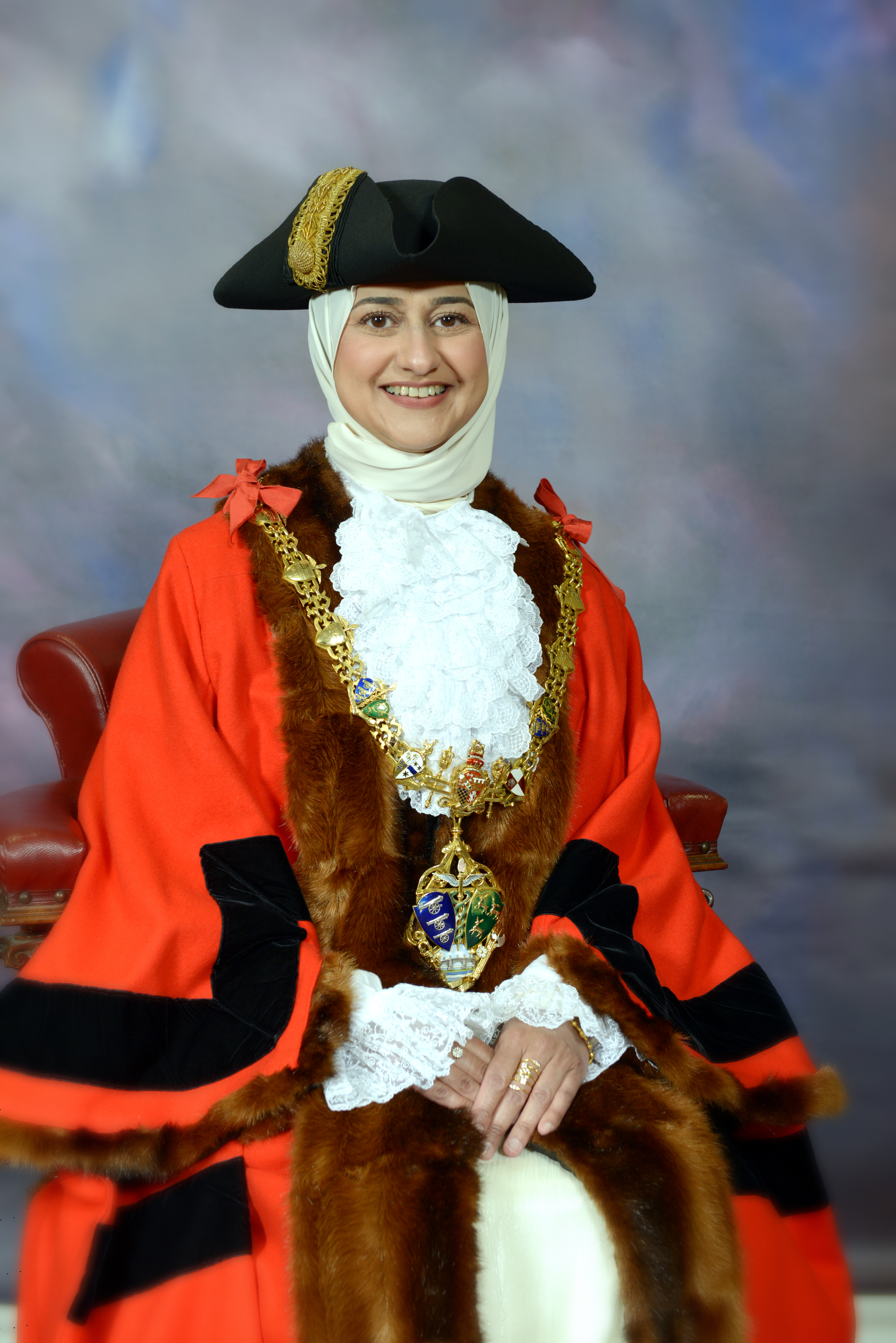 A woman sat in official mayoral clothing smiling at the camera.