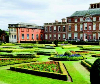 A house in the background with a garden shown with colourful flower beds.