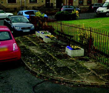 At the side of a rusting gate there is a wooden bench and concrete flower planters.