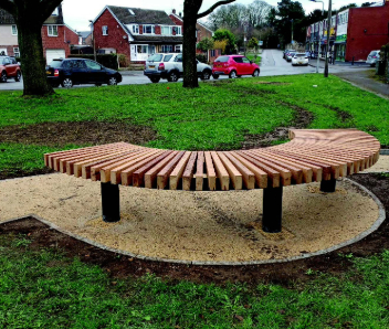 A curved light brown wooden bench on a path.