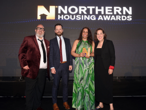 Two men and two women stood on a stage smiling. One of the women is holding a glass award.