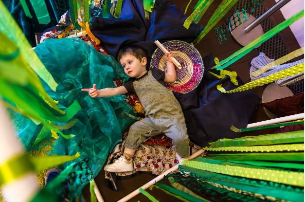 A child playing with green ribbon around them.