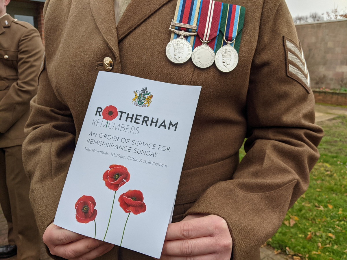 Close up of 2021 Rotherham Remembers order of service, held by a soldier in brown uniform with medals on their chest