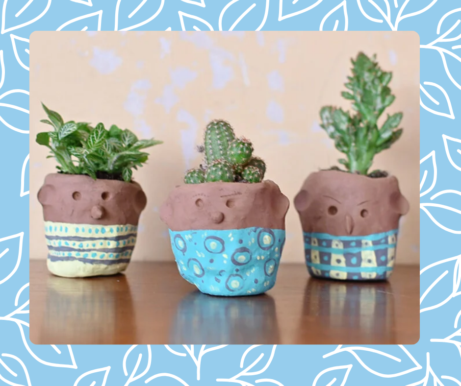 Three brown clay pots with faces on them, a blue bottom half and green plants in them, sit on a brown table with a beige background.