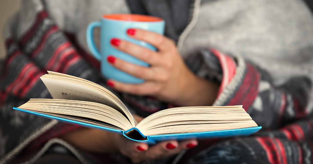 A person reading with a cup of tea and blanket