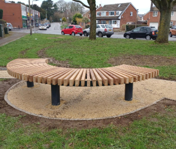 A curved bench on a path with grass surrounding it.