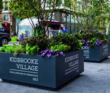 A grey flower box is shown on a grey pebbled street.