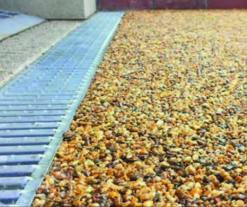 A close up of orange and black gravel next to a silver drain.