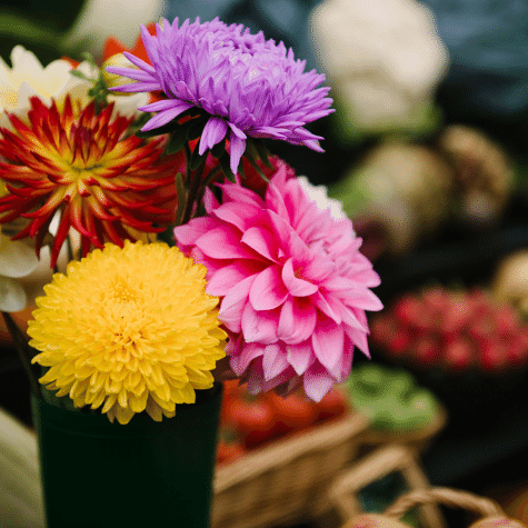 A vase of dahlias and in the background displays of vegetables and fruit.