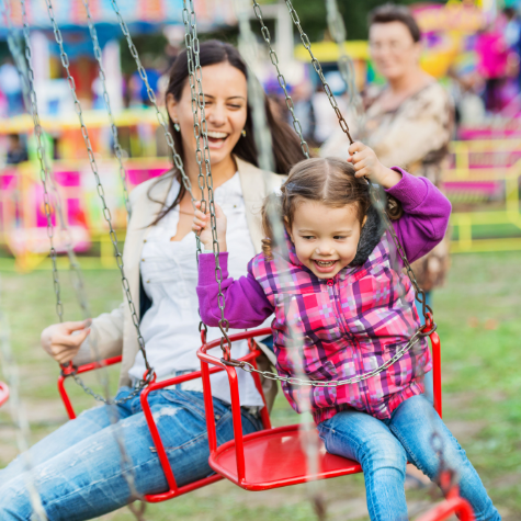 Mother and young daughter laughing on a fair ground ride.