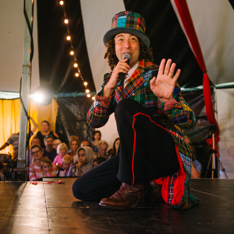 A brightly dressed performer in a striped big-top marquee.