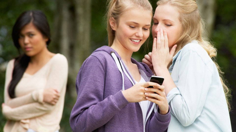 two girls talking with girl excluded in background