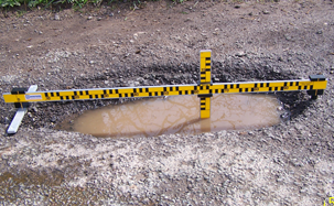 A deep pothole with a piece of measuring equipment stretched over it.