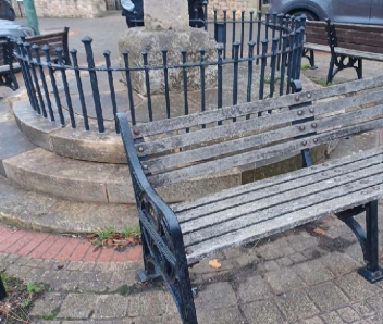 A brown wooden bench with a black footer in front of the Cenotaph.