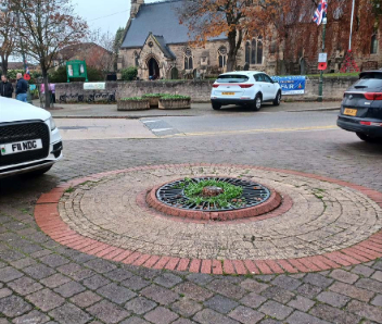 A tree pit with grey stones in the middle and orange bricks around the outer edge.
