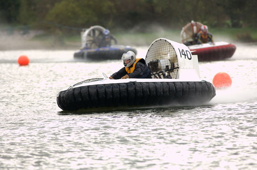 Three people racing in hovercrafts on water.
