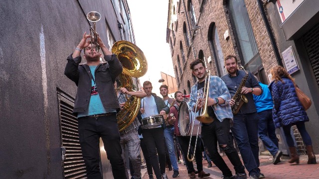 Hyde Park Brass playing whilst walking down urban street