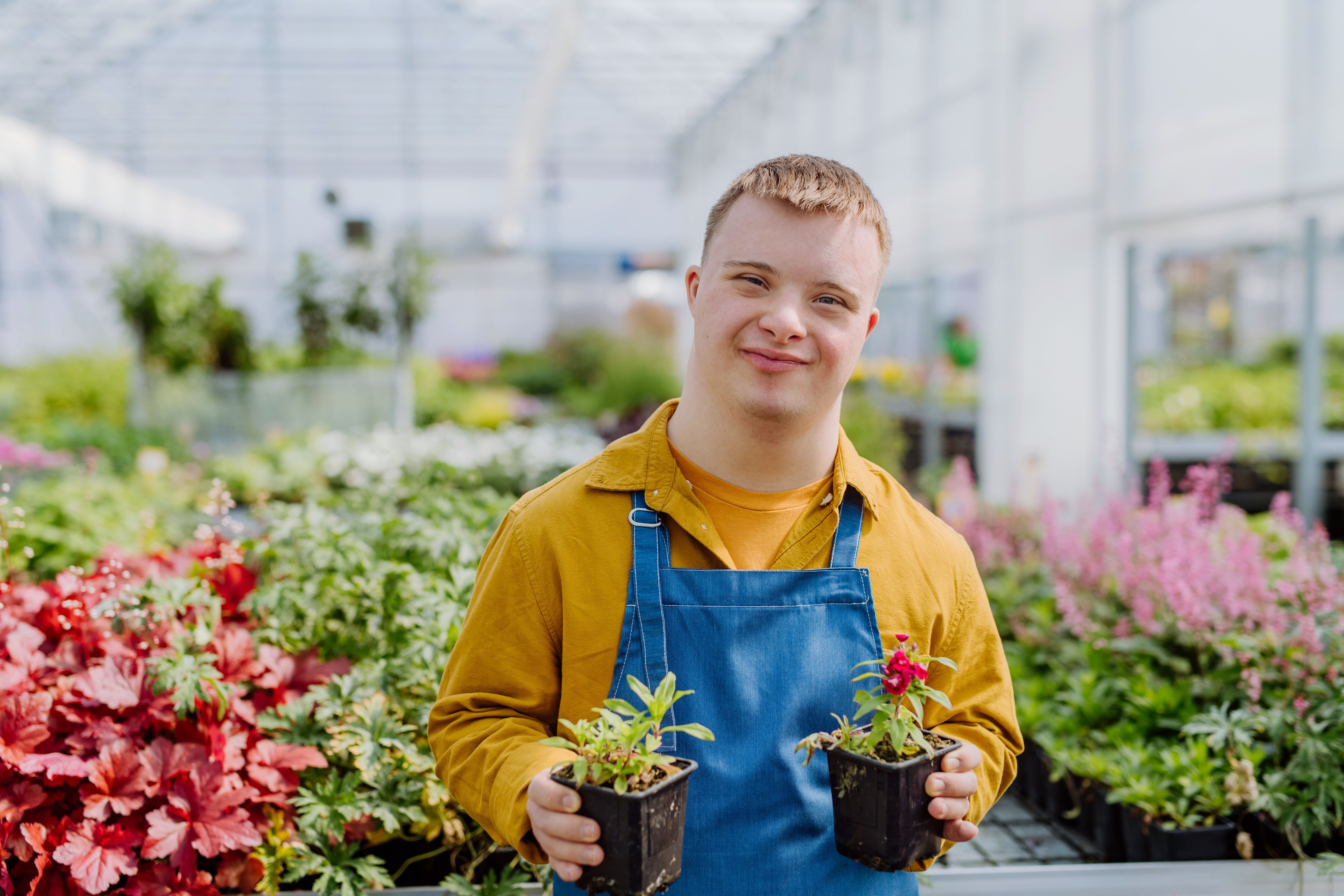 Young male with learning disabilities holding two plants and stood inside a garden centre