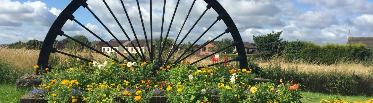 Photo of a mill wheel surrounded by flowers in bloom