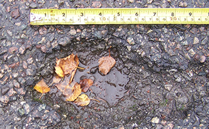 A small pothole, with a ruler laid face-up above the pothole.