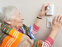 An elderly woman adjusts a thermostat