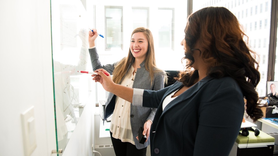 Two women writing on whiteboard